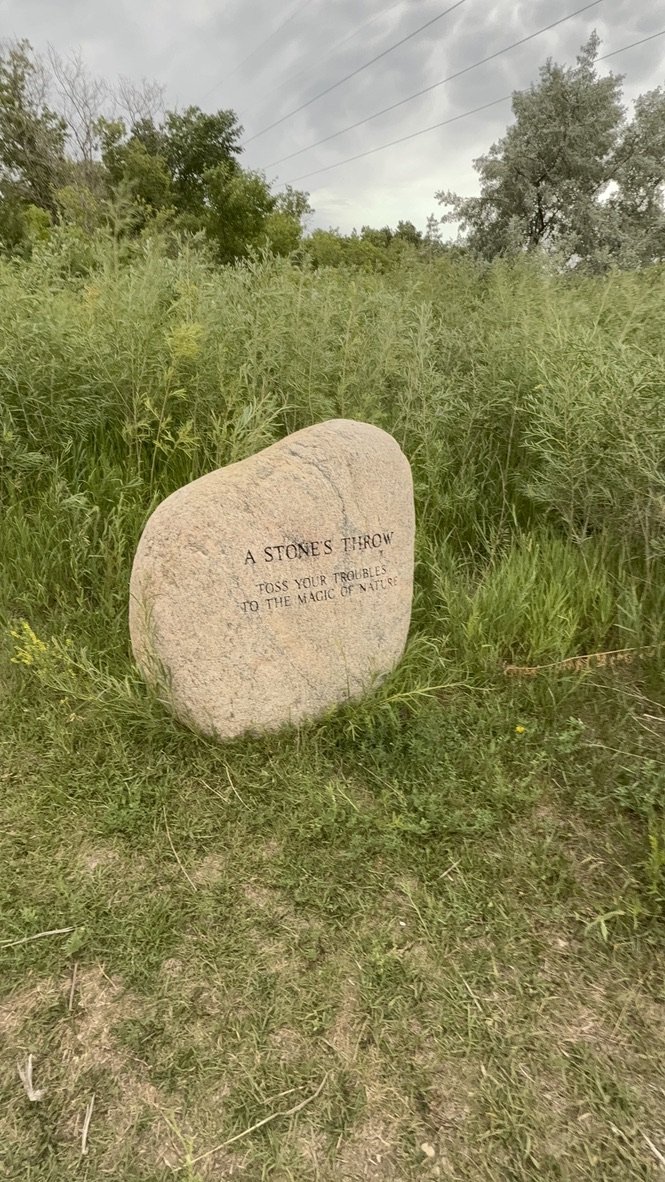 Large stone engraved with 'A Stone’s Throw – Toss Your Troubles to the Magic of Nature'