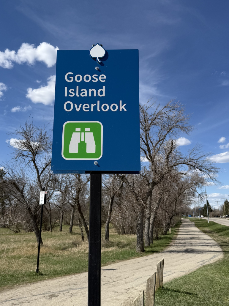 goose_island_overlook Blue Goose Island Overlook sign beside a paved pathway near Douglas Park hill under a bright blue sky.