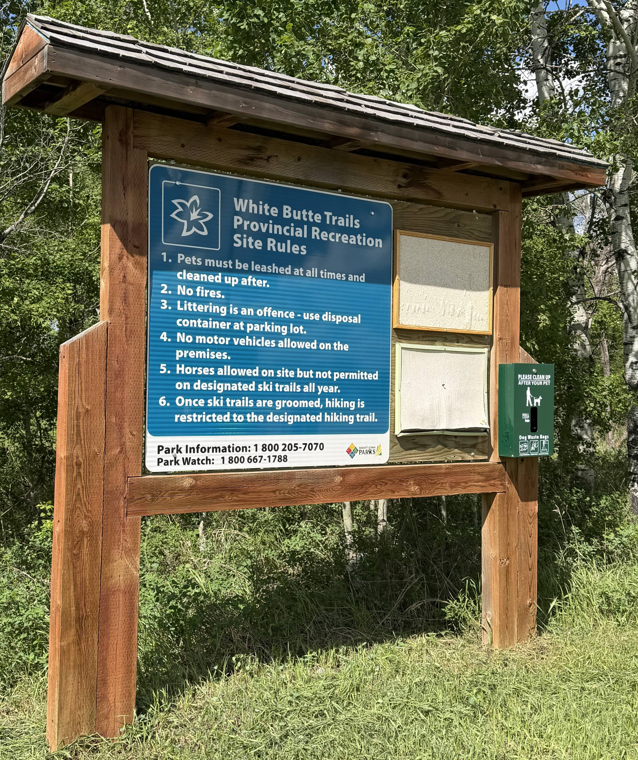White Butte Trails Provincial Recreation Site rules and information sign surrounded by trees.