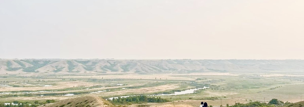 Hikers walking along a prairie ridge overlooking the South Saskatchewan River Valley at sunset.