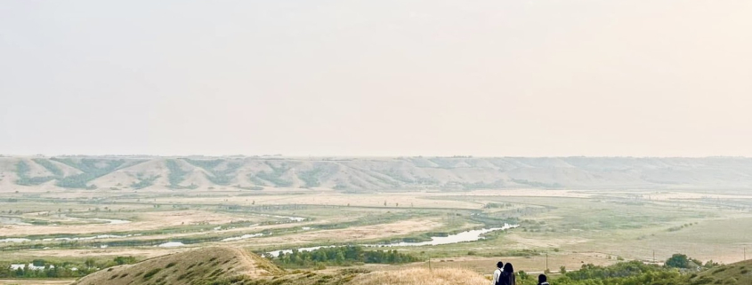 Hikers walking along a prairie ridge overlooking the South Saskatchewan River Valley at sunset.